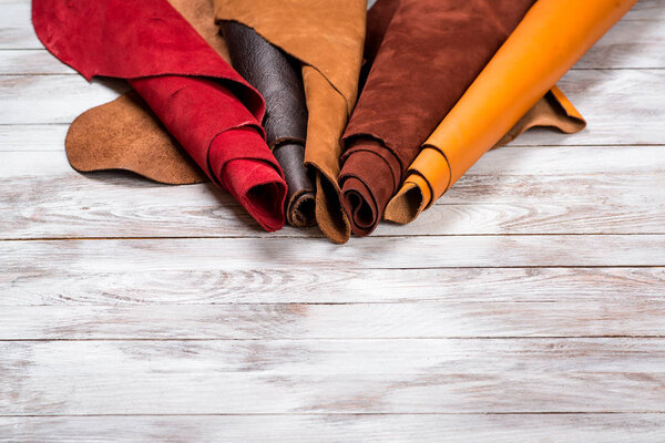 Brightly colored leather in rolls on white wooden background. Leather craft. Copy space.