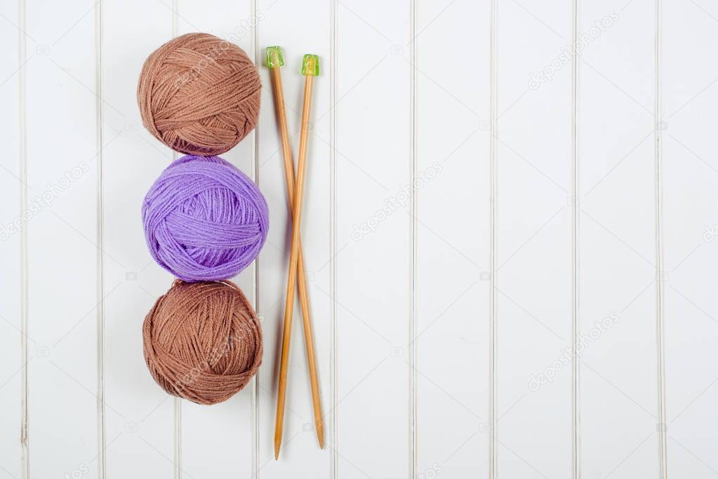 Knitting yarn balls and needles on the white wooden background.