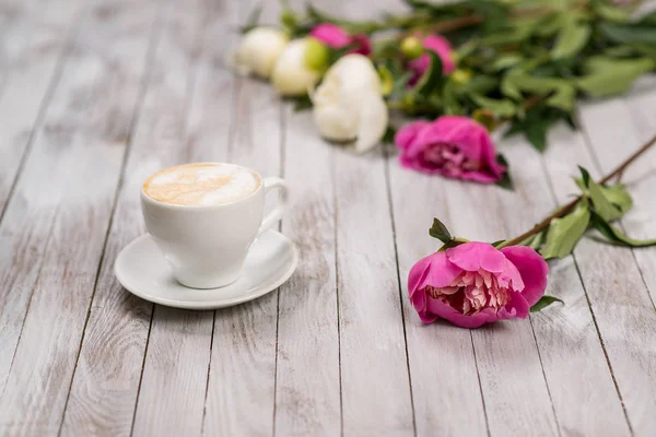 Un bouquet de pivoines et une tasse de café sur fond de bois clair . — Photo