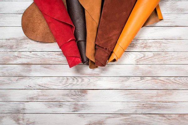 Brightly colored leather in rolls on white wooden background. Leather craft. Copy space. Top view. — Stock Photo, Image