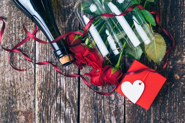 Bouquet di rose rosse, due bicchieri, bottiglia di vino, confezione regalo con etichetta su tavola di legno vintage. San Valentino. Vista dall'alto . — Foto Stock