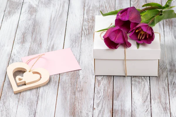 Frischer lila Tulpenstrauß und Geschenkbox auf Holzgrund. Raum für Text. Dekoratives Herz. — Stockfoto