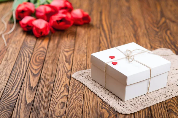 Roter Tulpenstrauß und eine Geschenkbox auf einem Holztisch. — Stockfoto