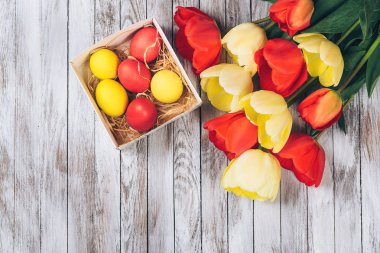 Renkli Paskalya yumurtaları ve Beyaz ahşap zemin üzerinde taze laleler.