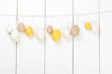 İpte asılı beyaz ahşap arka plan üzerinde renkli Paskalya yumurtaları.