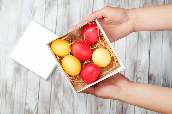 Les mains féminines tiennent une boîte cadeau de Pâques avec des œufs colorés . — Photo