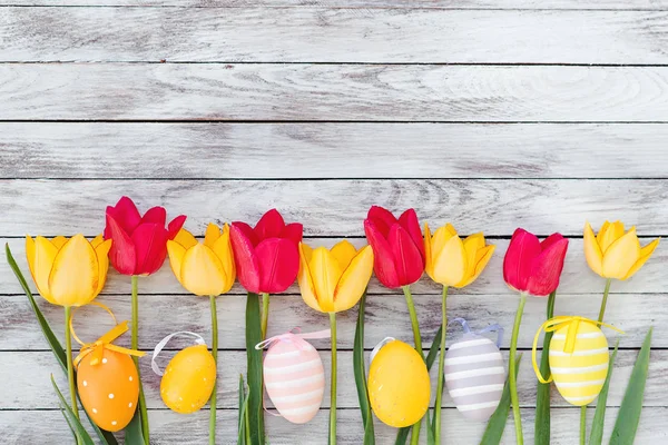Ovos de páscoa coloridos e tulipas em tábuas de madeira . — Fotografia de Stock