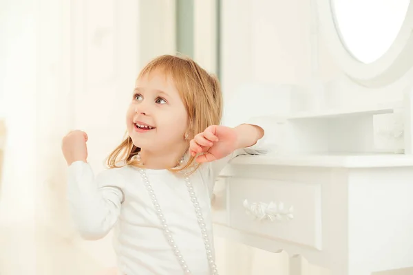 Porträt eines süßen kleinen Mädchens, das neben einem Spiegel im hellen Raum sitzt. — Stockfoto