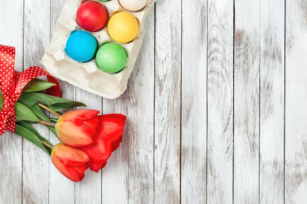 Oeufs de Pâques colorés et tulipes fraîches sur fond de bois blanc . — Photo