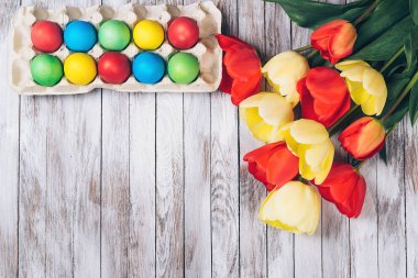 Renkli Paskalya yumurtaları ve Beyaz ahşap zemin üzerinde taze laleler.