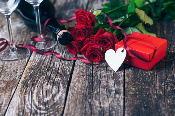 Букет з Троянди червоні, дві склянки, пляшку вина, подарунок коробку з тегом на старовинні дерев'яні дошки. День Святого Валентина. — стокове фото