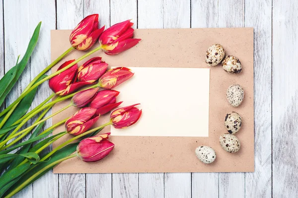 Huevos de Pascua, hermosos tulipanes rojos, nota en blanco sobre fondo de madera . — Foto de Stock