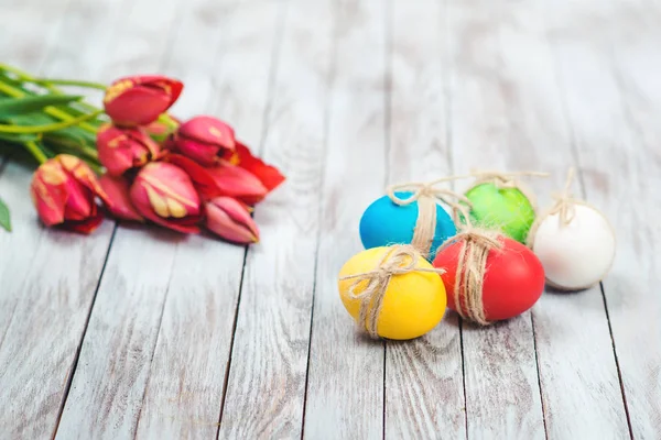 Oeufs de Pâques colorés, pot de fleurs avec herbe verte et belles tulipes sur fond en bois . — Photo