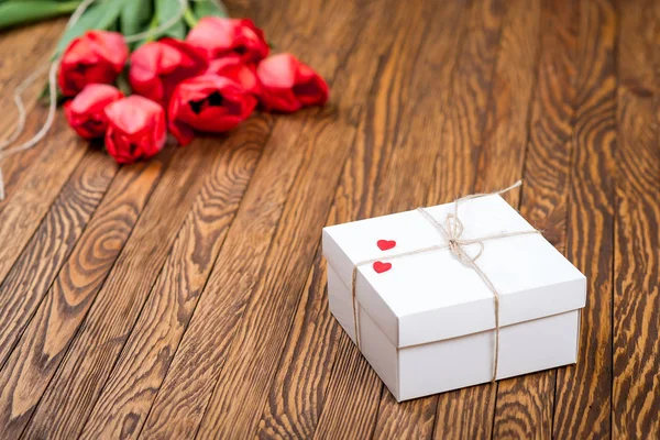 Roter Tulpenstrauß und eine Geschenkbox auf einem Holztisch. — Stockfoto