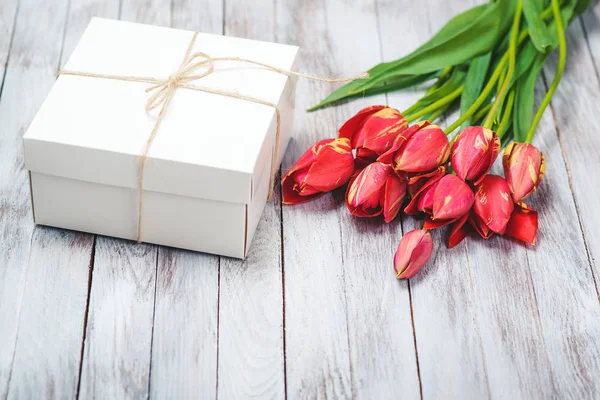 Gift box and tulips bouquet on shabby white wooden background. Space for text. Selective focus. — Stock Photo, Image