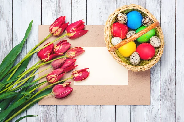 Œufs de Pâques, belles tulipes rouges, note blanche sur fond en bois . — Photo