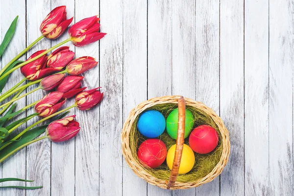 Fond de Pâques. Oeufs de Pâques colorés et tulipes rouges sur fond en bois. Vue de dessus. Espace pour le texte . — Photo