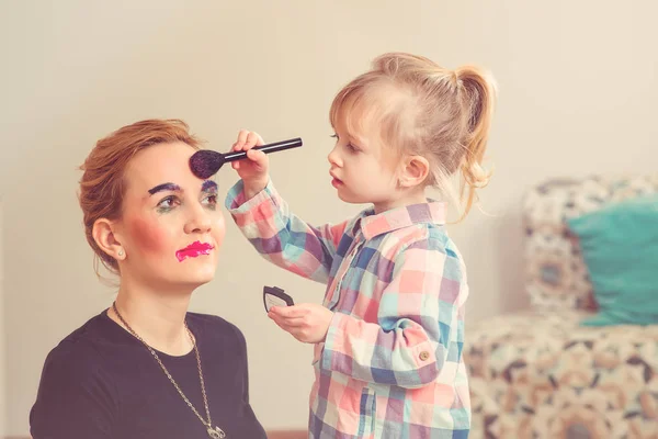Niedliche kleine Mädchen machen Make-up für ihre schöne Mutter. gemildert. — Stockfoto