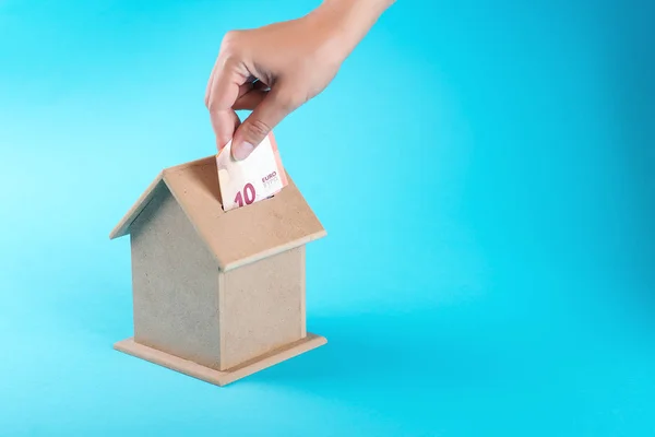 A female hand putting a ten euro into a money box. The concept of financial savings to buy a house.