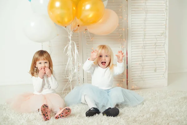 Niedliche kleine Mädchen in Kleidern, die zusammen in einem hellen Raum spielen. Happy Birthday Konzept. — Stockfoto