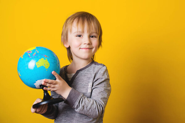 Smiling little boy holding globe in hands - isolated on yellow.