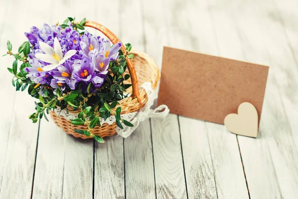 Lindas flores de croco em uma cesta perto de cartão vazio para o seu texto sobre fundo de madeira. Tonificado . — Fotografia de Stock