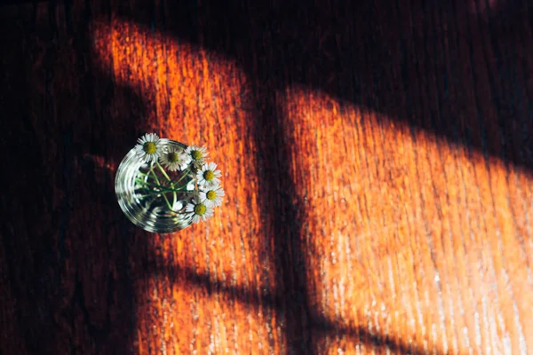 Petites marguerites dans un vase en verre sur un fond en bois . — Photo