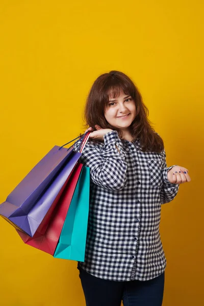 Mujer feliz de tamaño grande sosteniendo bolsas de compras de colores sobre fondo amarillo . — Foto de Stock
