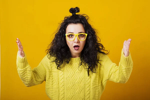 Mujer joven sorprendida en gafas con peinado moderno sobre fondo amarillo . — Foto de Stock
