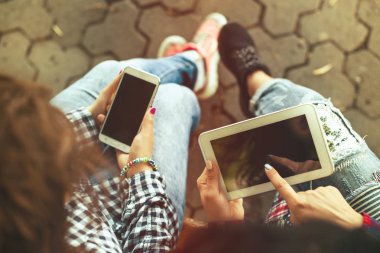 Telefon ve tablet bilgisayar açık havada olan iki genç kadın. Tonda.