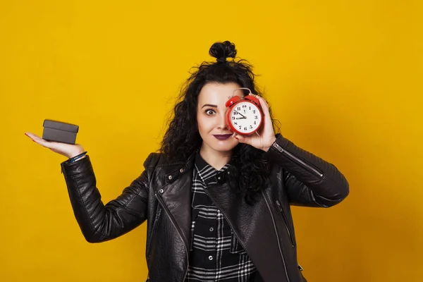 Mujer joven y elegante sosteniendo una caja de regalo en una mano y reloj despertador ante su cara, frente al fondo amarillo . — Foto de Stock