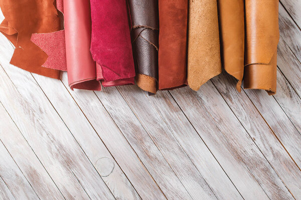 Multicolored leather in rolls on wooden background.