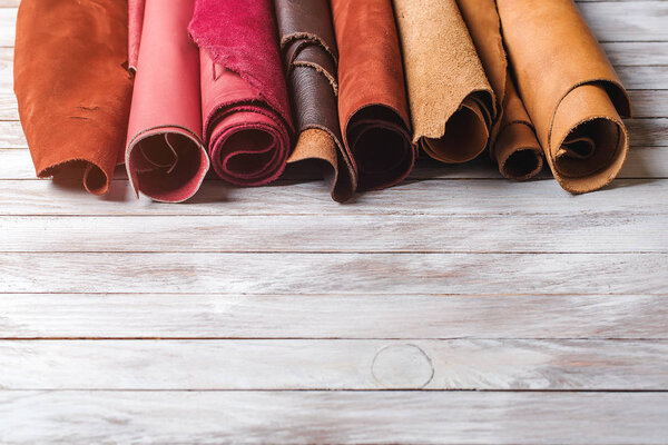 Multicolored leather in rolls on wooden background.