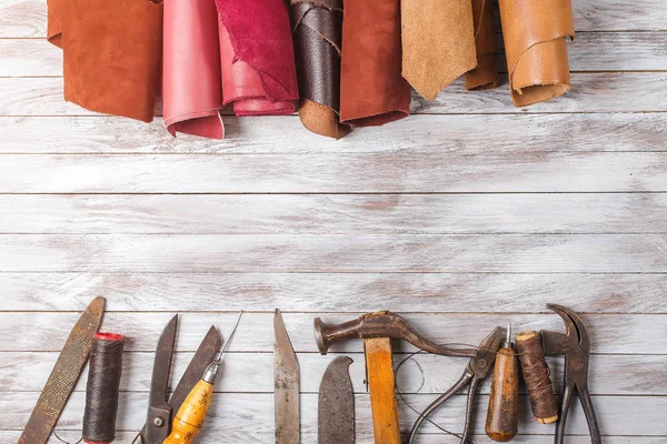 Set of cobbler tools and a lot of brightly colored leather in rolls on wooden background. Space for text. — Stock Photo, Image