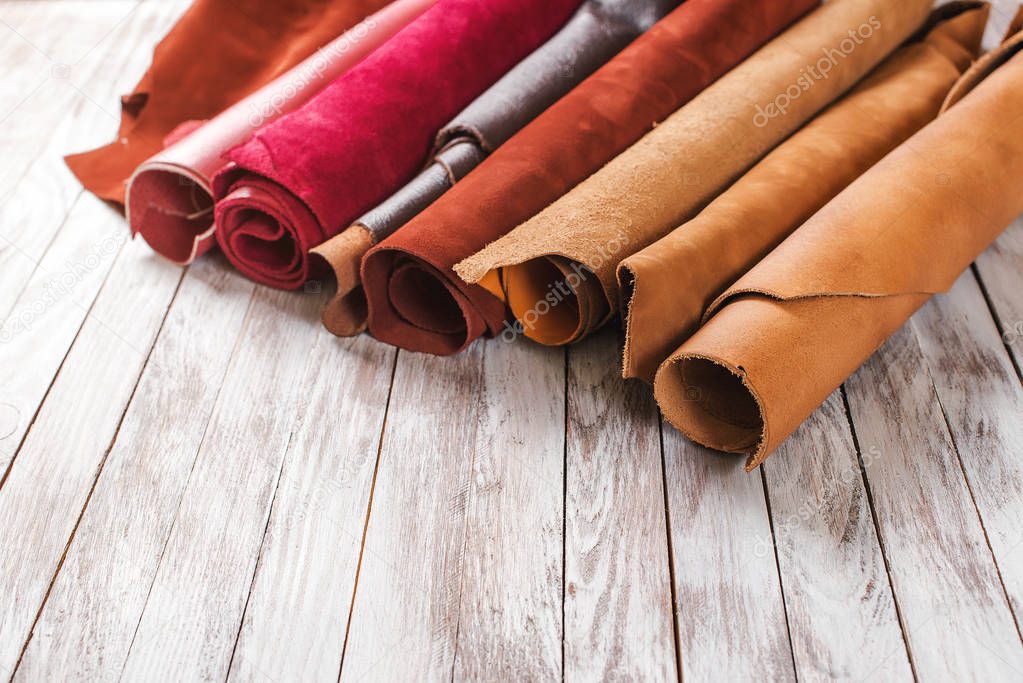 Multicolored leather in rolls on wooden background.