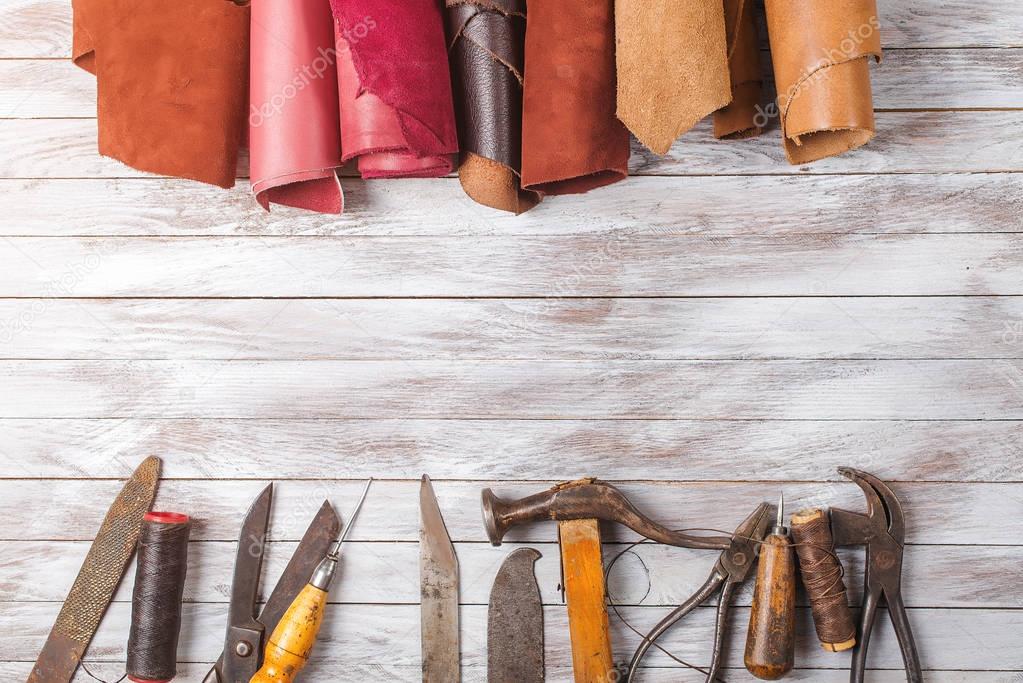 Set of cobbler tools and a lot of brightly colored leather in rolls on wooden background. Space for text.