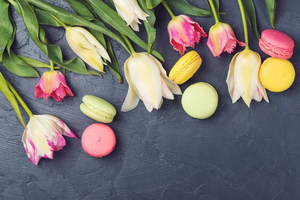 Colorful tulips and macaroons on black background. Top view. — Stock Photo, Image