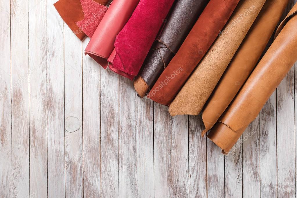 Multicolored leather in rolls on wooden background.