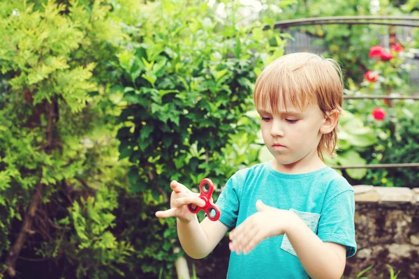 Leuke jongen spelen met Tri Fidget Hand Spinner outdoors. Trendy speelgoed voor handen voor kinderen en volwassenen. — Stockfoto