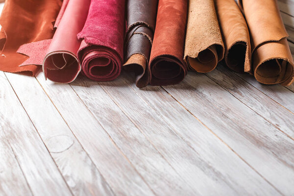 Multicolored leather in rolls on wooden background.