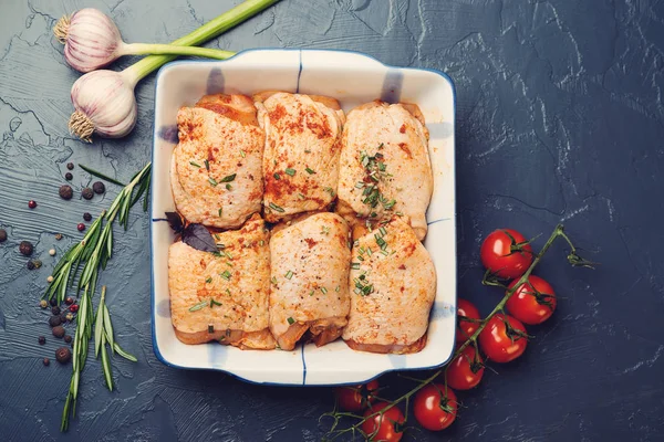 Caderas de pollo fresco marinado en un tazón con ingredientes de cocina sobre fondo negro . — Foto de Stock