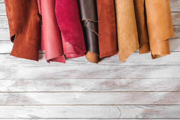 Multicolored leather in rolls on wooden background. — Stock Photo, Image