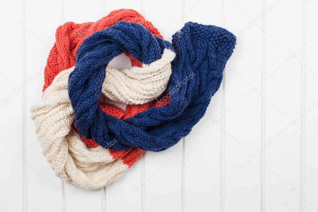 Colorful woolly hat and scarf on white wooden background.