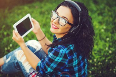 Tablet pc ve müzik açık havada için dinlerken kulaklık kullanarak mutlu güzel kız.