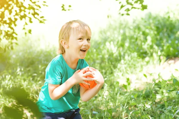 Χαριτωμένο χαμογελαστό αγόρι παίζει με πολύχρωμη μπάλα στον κήπο, ηλιόλουστη μέρα. Έννοια άθλημα και διακοπές. — Φωτογραφία Αρχείου