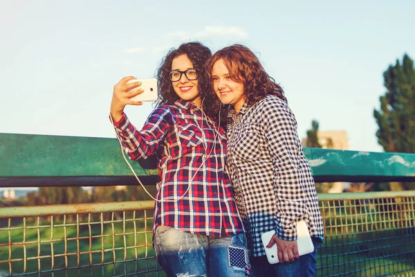Dos chicas novia tomar una selfie en el teléfono inteligente y escuchar música al aire libre . — Foto de Stock