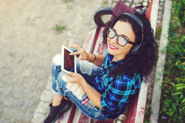 Счастливая симпатичная девушка с планшетным компьютером и наушниками, слушая музыку на улице . — стоковое фото