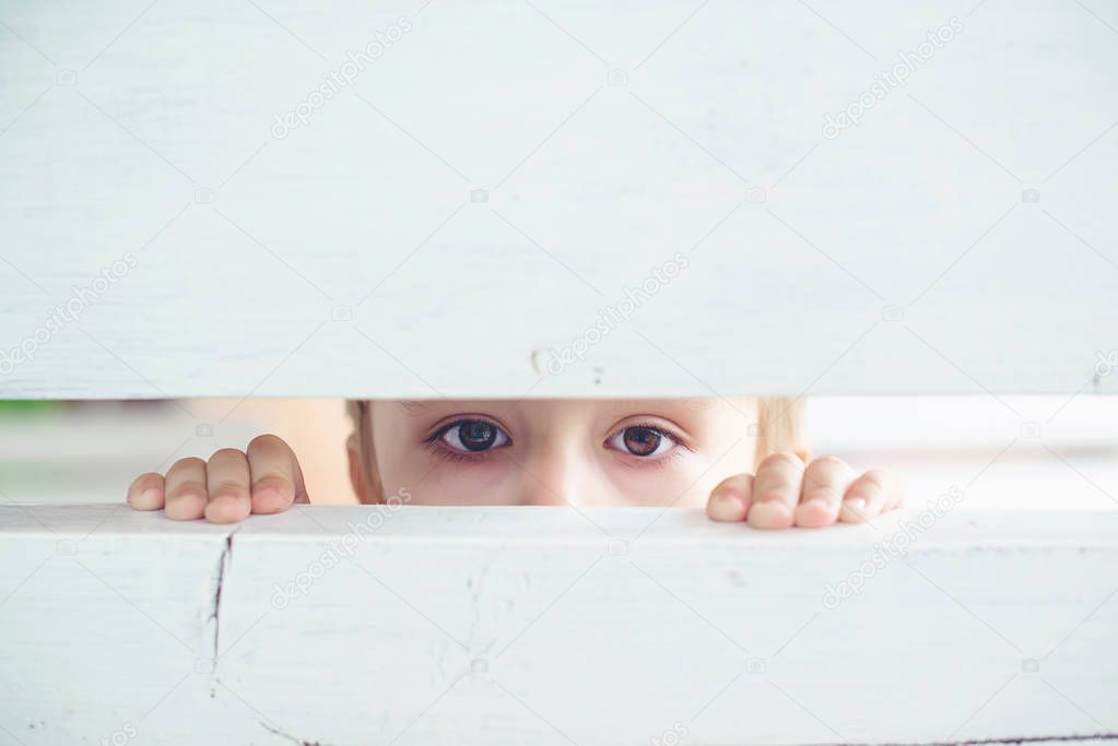 Sad little boy looks through the fence slit, view from ambush.