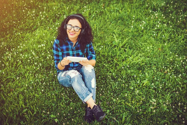 Gelukkig mooi meisje met behulp van de tablet pc en koptelefoon luisteren naar muziek in openlucht. — Stockfoto