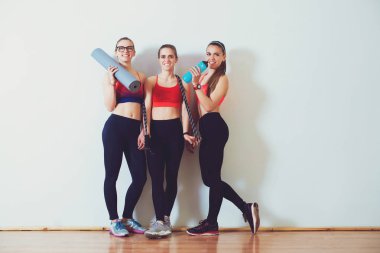 Fitness salonunda spor giyim ayakta karşı üç fitness genç kız duvar. Gülümseyen ve kamera için arayan kızlar.